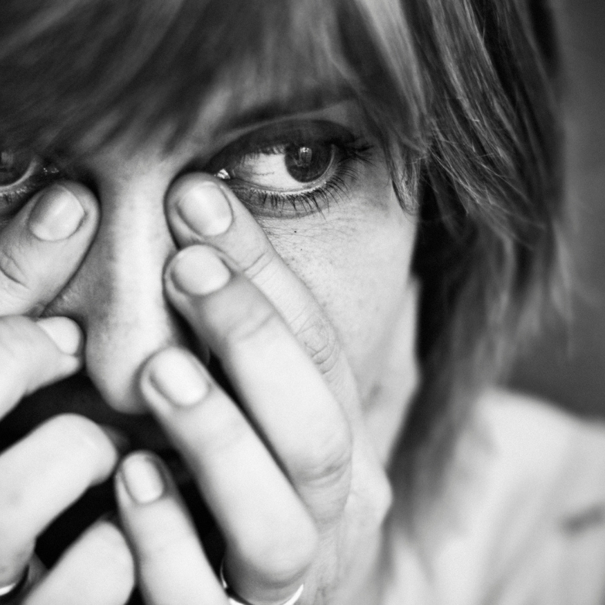 Close-up of anxious woman covering her face with hands, eyes wide with emotion symbolising fear of abandonment and nervous system activation. From an article on nervous system healing by Tess Rene Coaching.