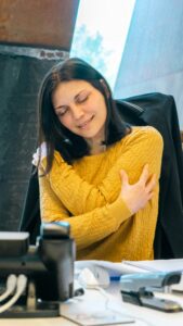 WOMAN IN YELLOW SWEATER GIVING HERSELF A HUG DEMONSTRATING SELF ACCEPTANCE AND LOVE