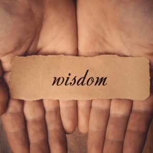 Person holding a paper that says 'wisdom' on it. symbolizes listening to your inner voice. For an Article on self-trust by Tess Rene Coaching.