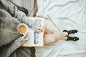 woman with tea and book on bed self-worth illustrating the build of self-worth. From an article by Tess Rene Coaching.