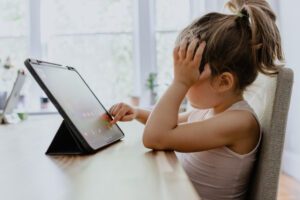 Little girl using a tablet, resting her head in her hand, symbolising emotional overwhelm — as discussed in Tess Rene Coaching’s gentle somatic practices guide