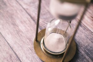 Hourglass on wooden table, symbolising patience and time, in article on acceptance by Tess René Coaching.
