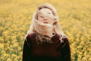 Woman standing in a yellow field, hair blowing in wind, symbolising playful presence and joy — part of Tess Rene Coaching’s writing on micro-moments