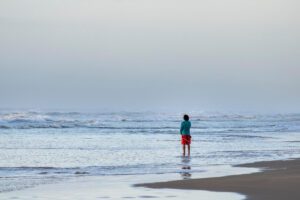 Person standing at ocean shore, symbolising solitude, accepting what is and self-compassion, in article on acceptance by Tess René Coaching.