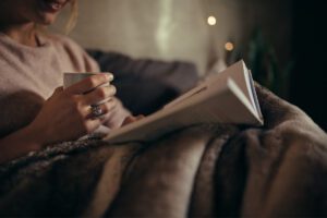 Woman resting with tea and a book, representing self-kindness and mental rest, in article by Tess René Coaching.
