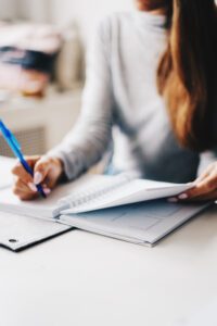 Close-up of a woman writing in a notebook with a blue pen, symbolising focus and reflection, from an article about relaxation by Tess Rene Coaching.