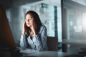 Woman holding her head in an office setting, used in an article by Tess René Coaching on accepting what is and calming unwanted thoughts