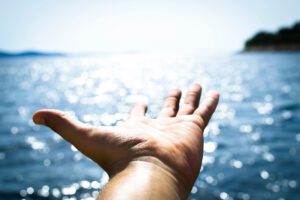 Hand reaching over sparkling water, illustrating acceptance that perfectionism will always resurface, in an article by Tess René Coaching.