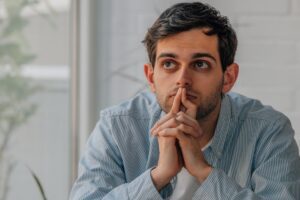 Why am I indecisive in relationships and work Man sitting in thought with hands clasped under chin, reflecting on hidden beliefs that shape decisions and can cause indecisiveness, in an article by Tess René Coaching about core beliefs.