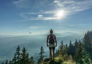 Person standing at a mountain edge looking toward the horizon, symbolising courage in uncertainty, in a Tess René Coaching article about facing fear.