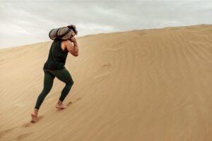 Man climbing a sand dune with a bag, representing resilience through imperfection in Tess René Coaching’s article.