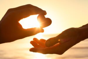 Hands sharing a heart at sunset, featured in this Tess René Coaching article about sharing joy and connection.