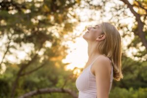 Woman outside breathing deeply in sunlight, shown in an article by Tess René Coaching on letting go of how life should be and practising accepting what is