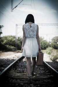 Woman walking alone on train tracks carrying a suitcase, symbolising stalled movement under perfectionism, in an article by Tess René Coaching