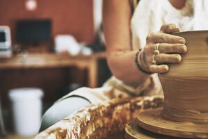 Clay-covered hands shaping a pot on the wheel, showing resilience over perfectionism in Tess René Coaching’s article.