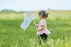 Child playing in tall grass with a net, shown in this Tess René Coaching article on joyful nature moments.