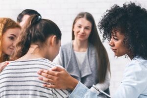 Supportive group scene with a hand on someone’s shoulder, reflecting outward compassion.