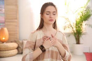 Woman with eyes closed and hands over her heart, modelling tender acknowledgement without wallowing.