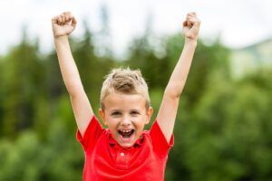 Happy child with arms raised in celebration, representing performance-based esteem highs.