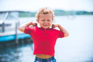 Smiling child flexing arms in a red shirt symbolising strength and resilience in an article by Tess René Coaching about training your brain like a muscle.