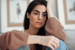 Woman sitting at home with hand on forehead, included in an article by Tess René Coaching on tribal roots of negative thinking and accepting what is