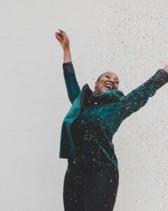 Woman laughing with arms raised as confetti falls, symbolising joy, confidence, and self-acceptance in this Tess René Coaching article about building self-worth