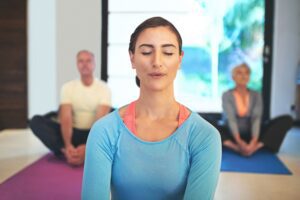 Woman in blue practising meditation in a calm indoor setting during a group class, from a Tess René Coaching article on managing emotions when life feels overwhelming