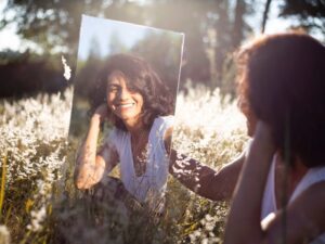 Woman smiling into a mirror in this Tess René Coaching article on maintaining self-worth after losing a friend.