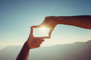 Hands framing the sun symbolising reframing and focus in this Tess René Coaching article about solution-focused thinking.