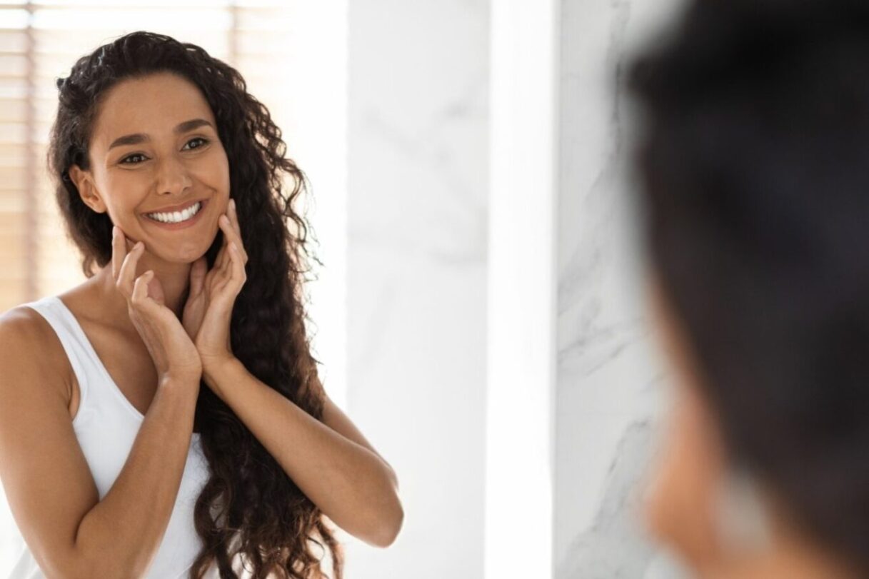 in this Tess René Coaching article about reparenting, a woman looks at herself kindly in the mirror, symbolising inner nurturing