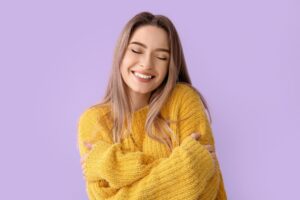 featured in Tess René Coaching’s inner child article, a woman smiles with eyes closed and hugs herself, symbolising inner peace.