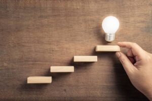 Wooden steps leading toward a lightbulb in this Tess René Coaching article about moving forward with solution-focused thinking even if it's imperfect or small.