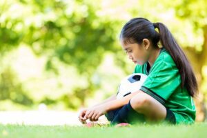 Young girl sitting with a soccer ball, reflecting quietly in a Tess René Coaching article about boundaries and belonging.