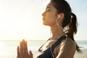 A woman standing calmly by the ocean with eyes closed, practising grounding and emotional regulation in this Tess René Coaching article.