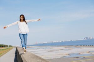 Woman balancing on a low wall by the ocean, symbolising steadiness through uncertainty, in article by Tess René Coaching about how to stop catastrophizing