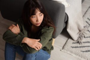 Woman sitting on floor with folded arms, reflecting on anxious thoughts, in article by Tess René Coaching about using CBT and somatic tools to stop catastrophizing