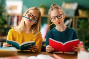 two girls laughing with pencils balanced on their faces symbolising playful learning and growth in Tess René Coaching article