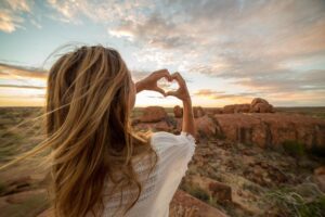 Woman forming a heart shape with her hands at sunset, symbolising healing let downs through embodiment in an article by Tess René Coaching