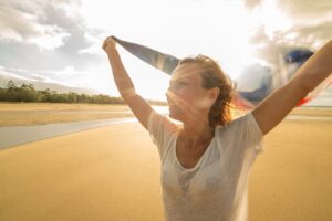embodied heart opening practice shown in this Tess René Coaching article with a woman lifting her arms in sunlight on a beach