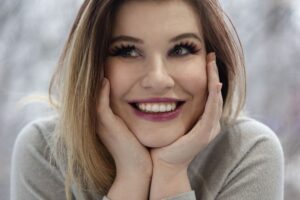 A woman with a soft joyful smile resting her face in her hands, shown in an article by Tess René Coaching about gratitude and opening the heart.