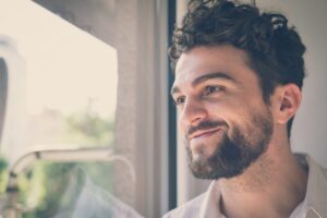 Man smiling as he looks out a window in a Tess Rene Coaching article about setting intentions to open the heart