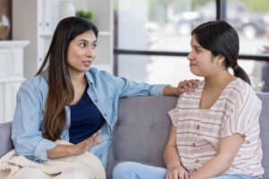 Two women talking on a sofa, one offering support to the other, illustrating how to address people who don’t support your change in this Tess René Coaching article.
