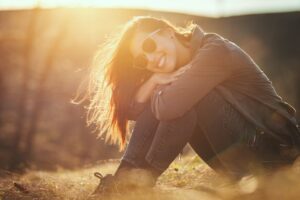 Smiling woman sitting in soft sunlight enjoying a quiet moment in this Tess René Coaching article about simple joyful ways to heal the nervous system