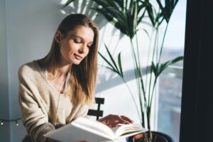 Woman reading calmly near natural light in an article from Tess René Coaching about simple ways to feel happier.