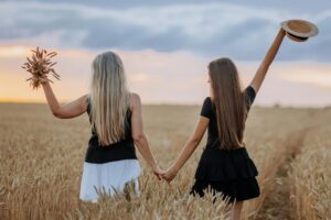 Two women walking hand in hand through a wheat field, representing how to normalise change and support new behaviour in this Tess René Coaching article.
