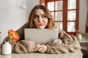 A woman resting her chin on her laptop looking unsure, illustrating adult patterns linked to childhood emotional neglect in a Tess René Coaching article.