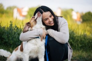 A woman hugging her dog in a grassy field, capturing a tender moment of joy in an article by Tess René Coaching.