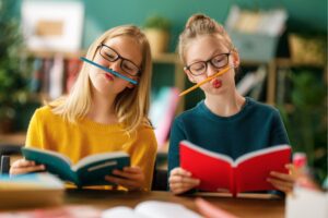 Two girls being playful while reading, in an article by Tess René Coaching about overcoming perfectionist standards.