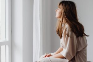 A woman looking out a bright window reflecting on childhood emotional neglect in an article by Tess René Coaching.