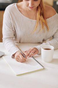 A woman writing in a notebook with tea beside her, used in this Tess René Coaching article on reparenting through thought.